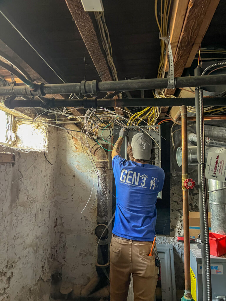 GEN3 Electric & HVAC technician performing Philadelphia home rewiring in a historic basement, organizing exposed wires and upgrading the electrical panel for safety.