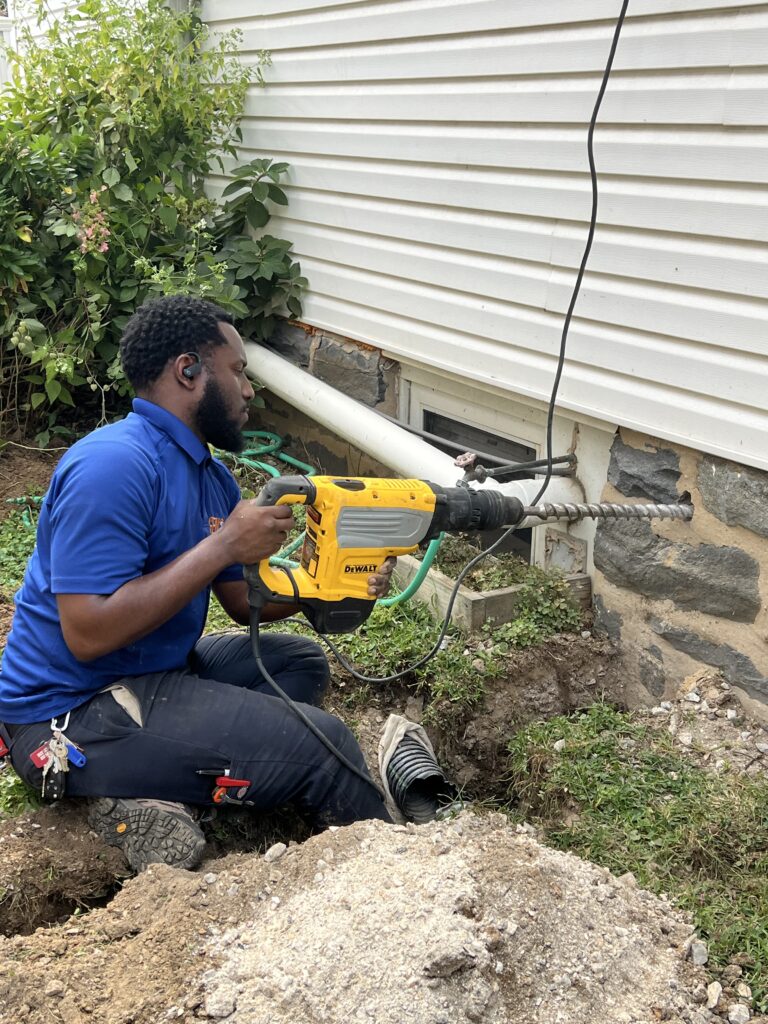 Electrician drilling into home foundation for detached garage subpanel installation in Philadelphia.