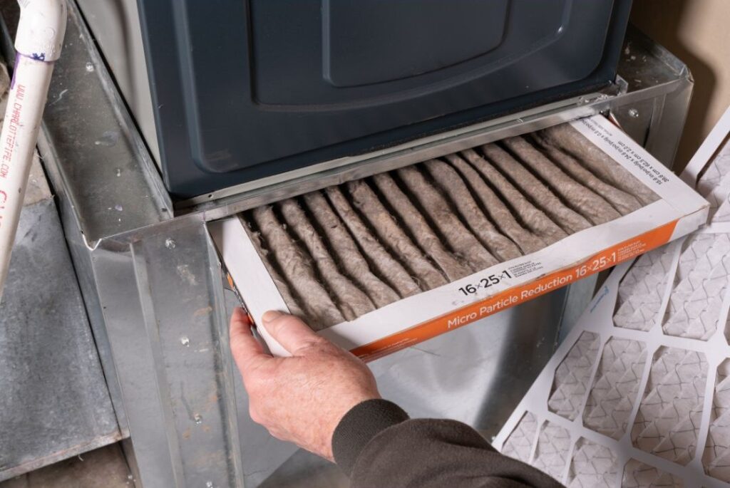 The pleated filter is covered in gray dust and debris, highlighting the need for replacement to maintain airflow and efficiency.