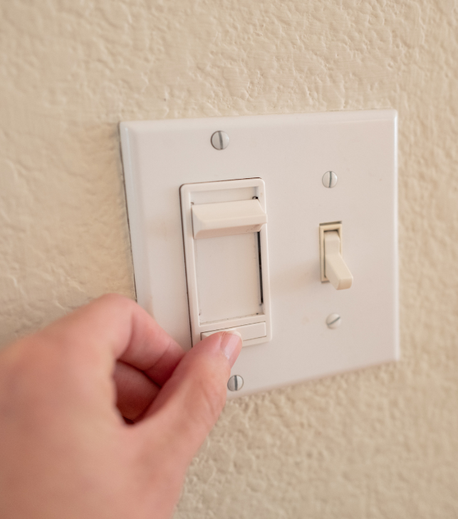 Close-up of a person adjusting a light dimmer switch on a wall plate beside a toggle switch